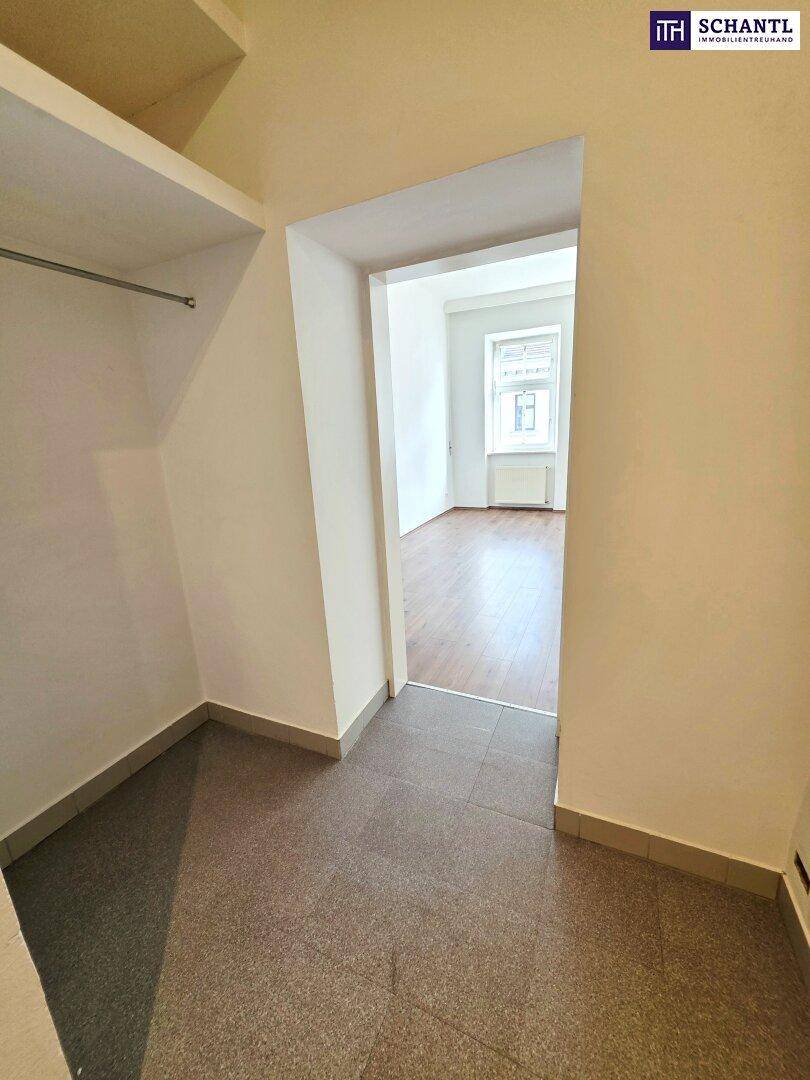 Praktischer Abstellraum mit Fliesenboden und Kleiderstange, angrenzend an ein Zimmer mit Holzboden.