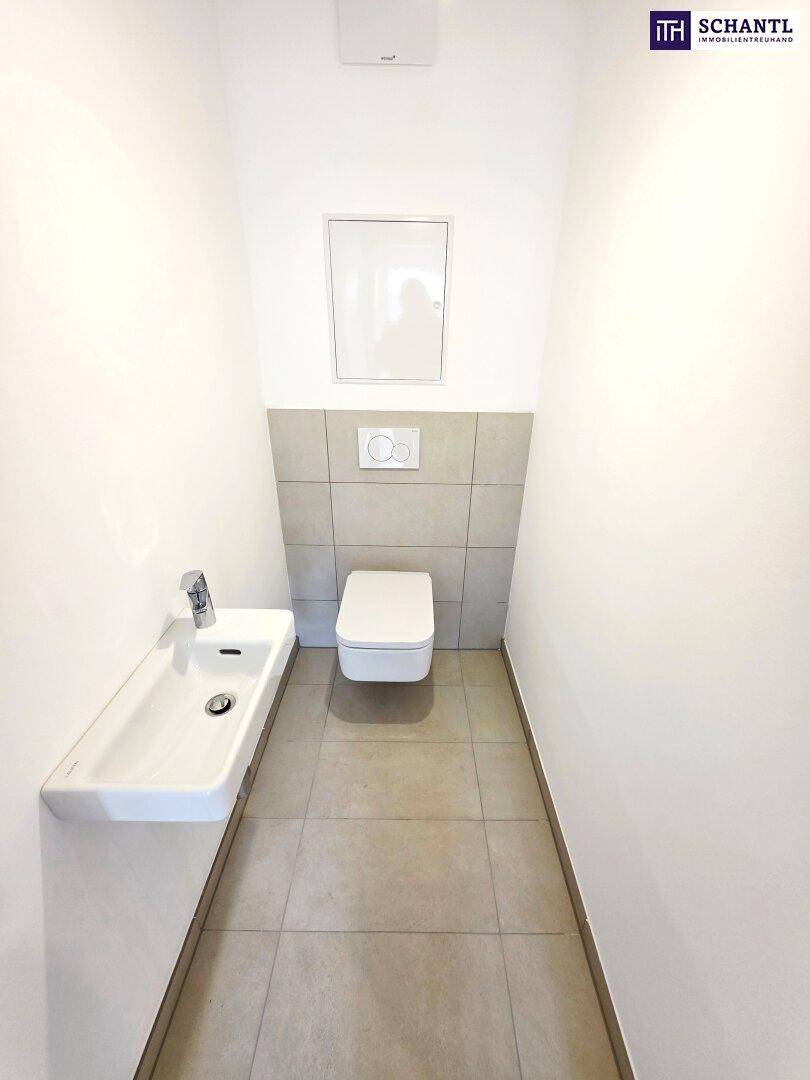 Modernes Gäste-WC mit Wand-WC, kleinem Waschbecken und hellen Fliesen.