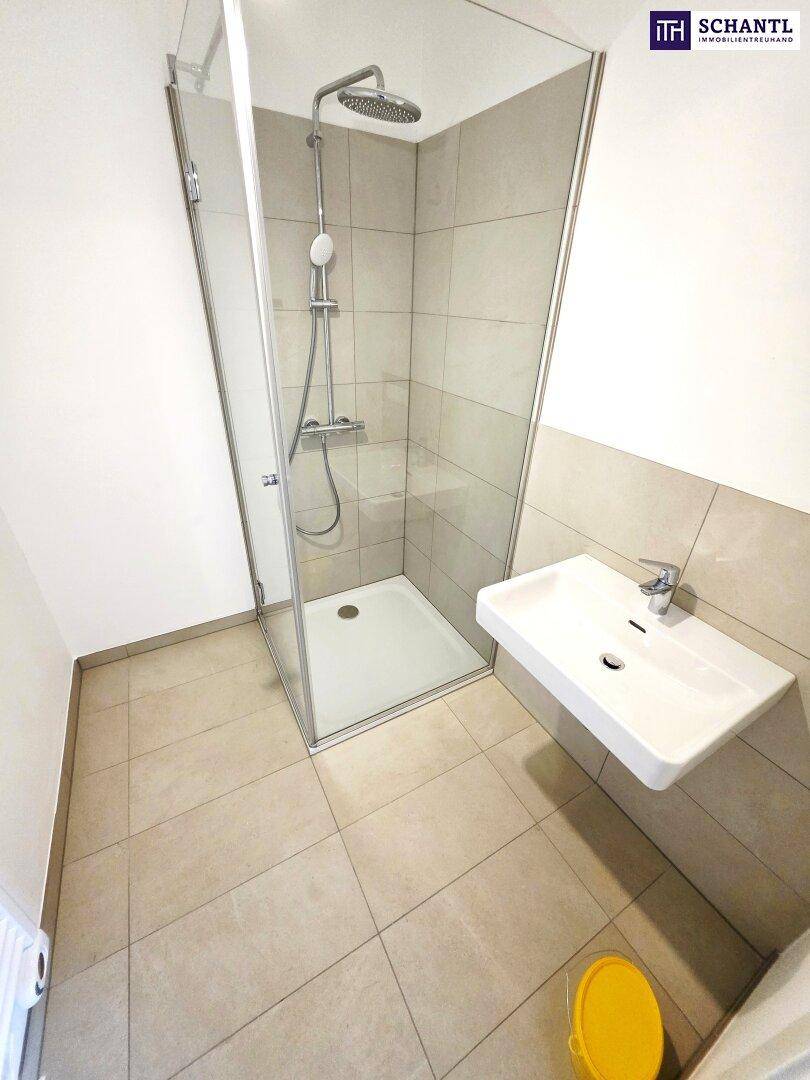 Modernes Badezimmer mit Duschkabine, Waschbecken und hellen Fliesen an Wänden und Boden.