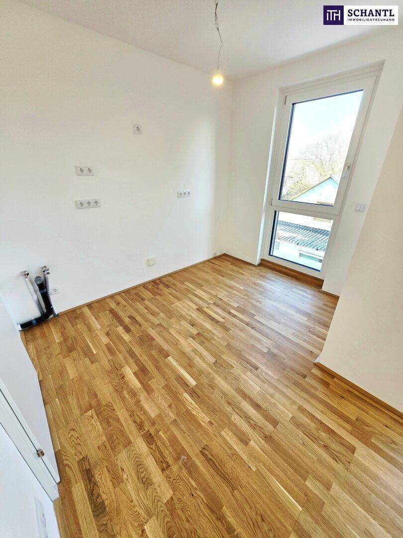 Helles Zimmer mit Parkettboden und Fenster, vorbereitet für eine mögliche Kücheninstallation.