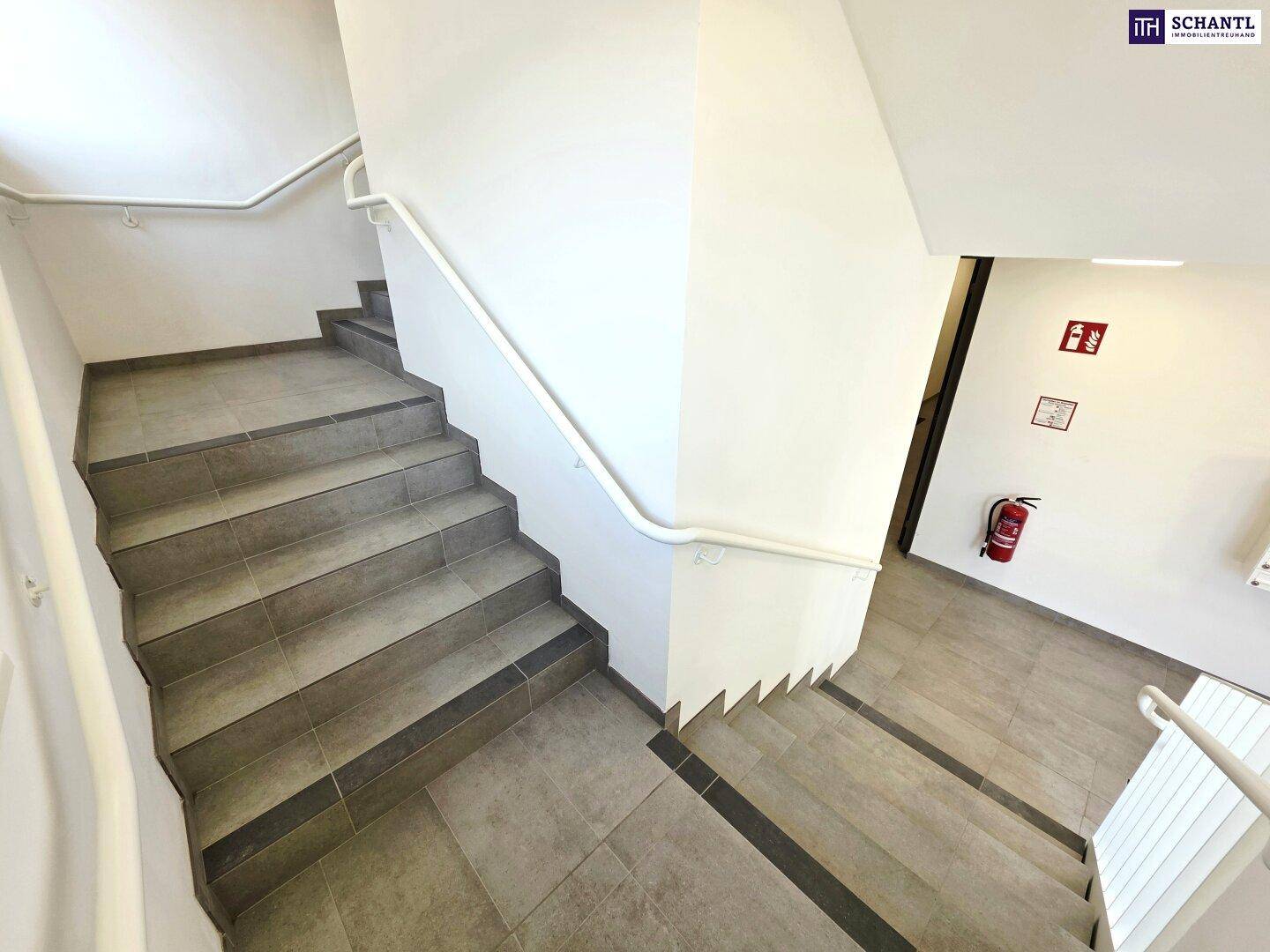 Treppenhaus mit Fliesenboden und weißem Geländer, führt zu den oberen Etagen.