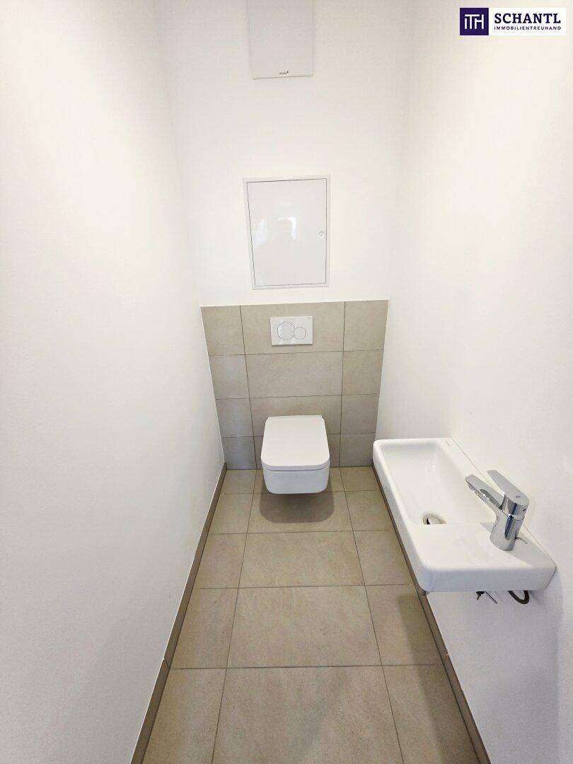 Modernes Gäste-WC mit wandhängender Toilette und kleinem Waschbecken, hell gefliest.
