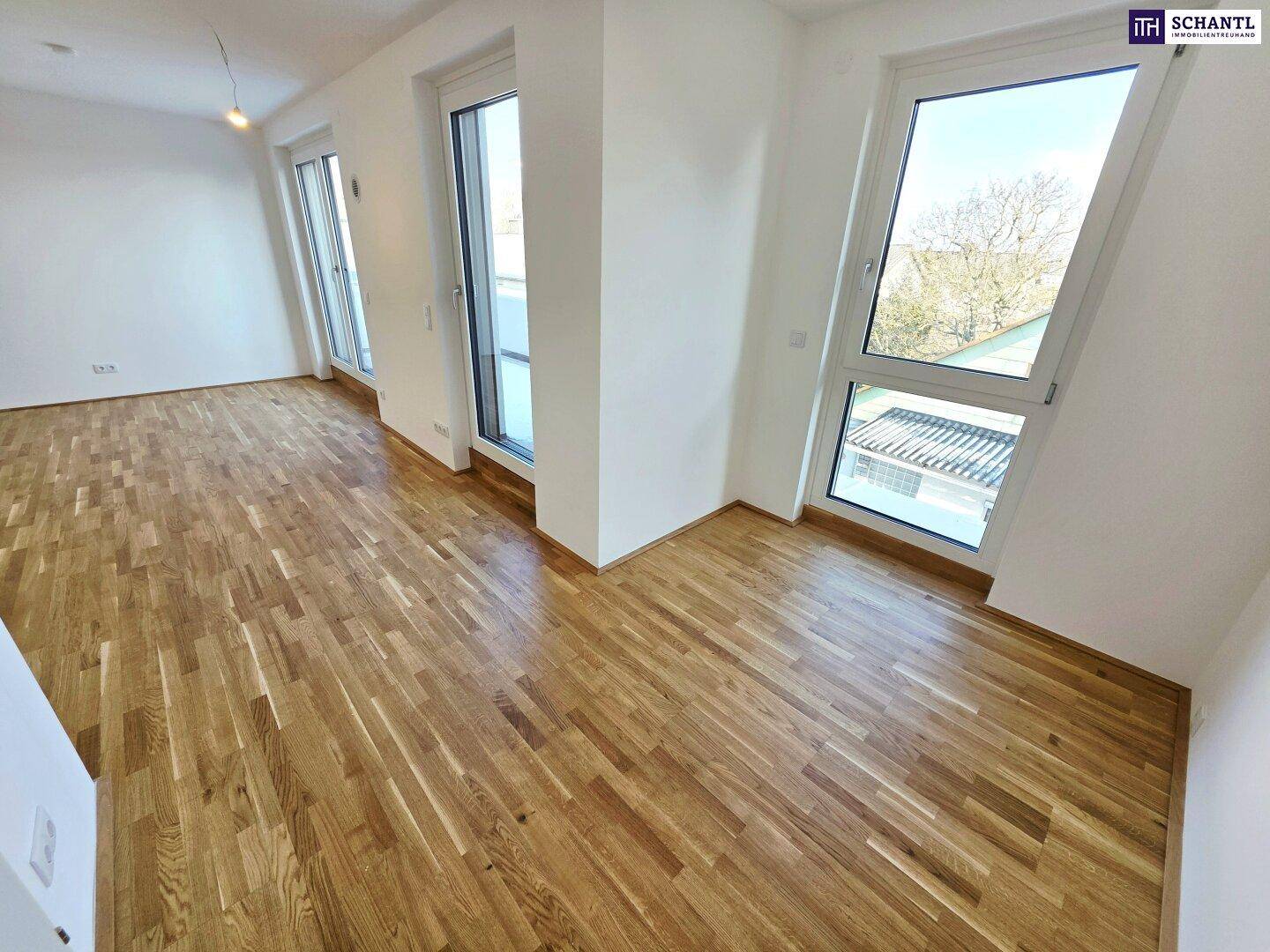 Heller Wohnraum mit Parkettboden und großen Fenstern, die viel Tageslicht hereinlassen.