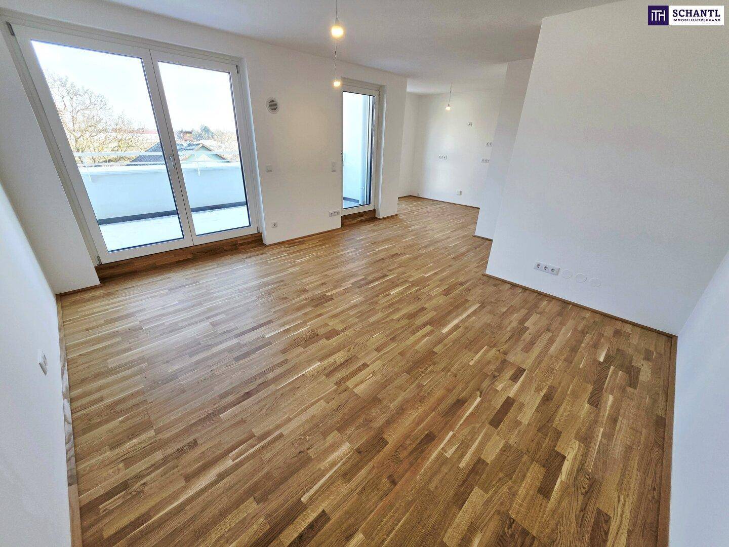 Helles Zimmer mit Parkettboden und großen Fenstern, die viel Tageslicht hereinlassen.