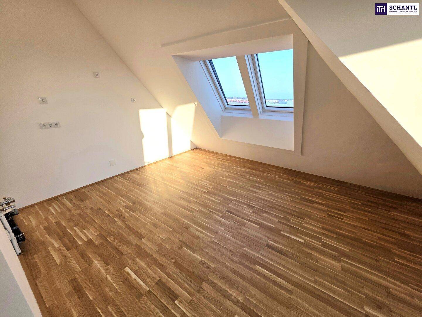 Geräumiges Zimmer im Dachgeschoss mit Holzboden und schrägen Wänden, beleuchtet durch Dachfenster.