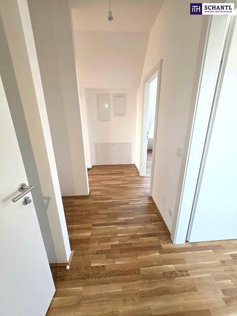 Heller Flur mit Holzboden und weißen Wänden, der zu weiteren Räumen führt.