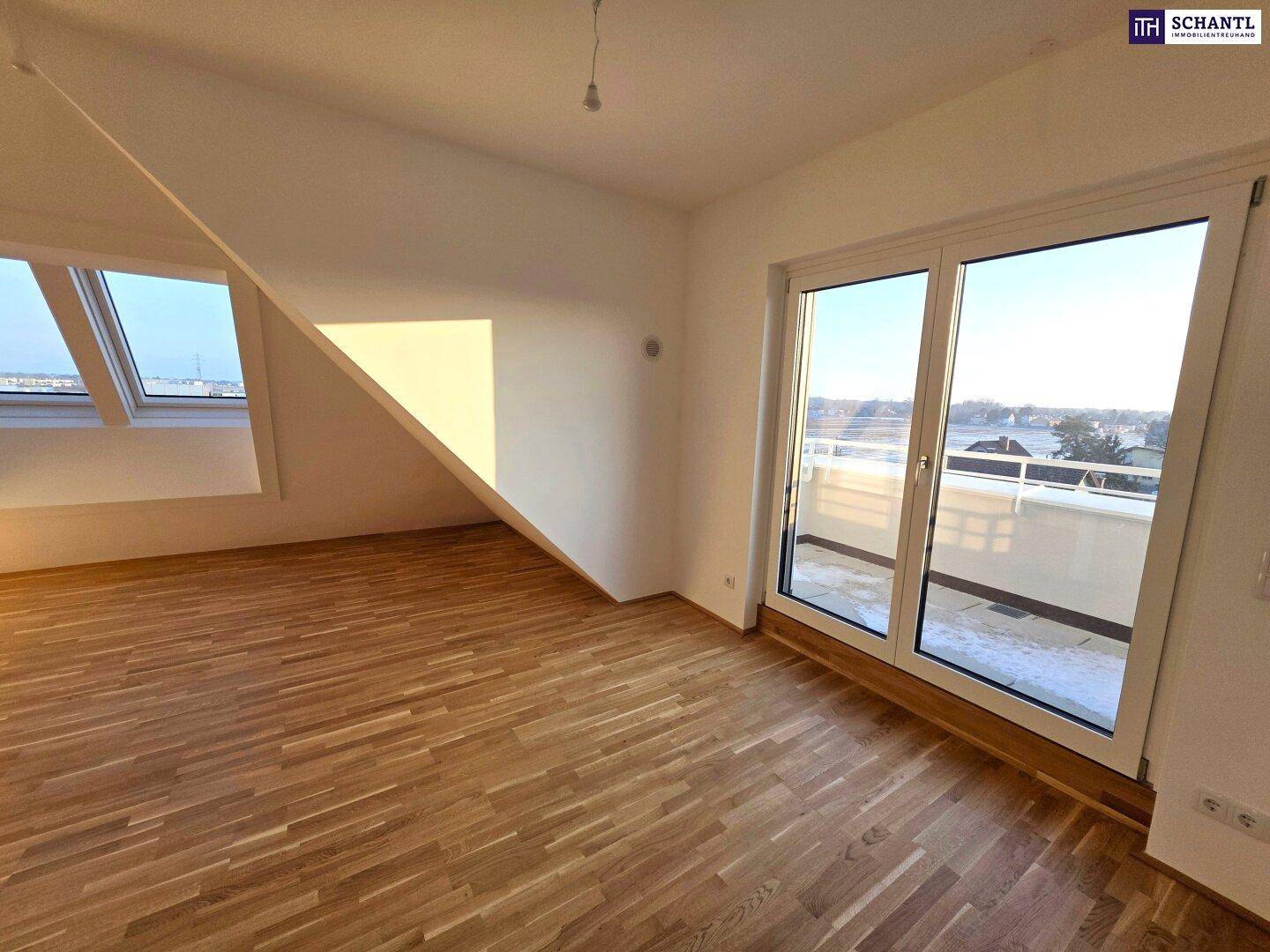 Helles Zimmer im Dachgeschoss mit Holzboden und großem Fenster mit Balkonzugang, sonnendurchflutet.