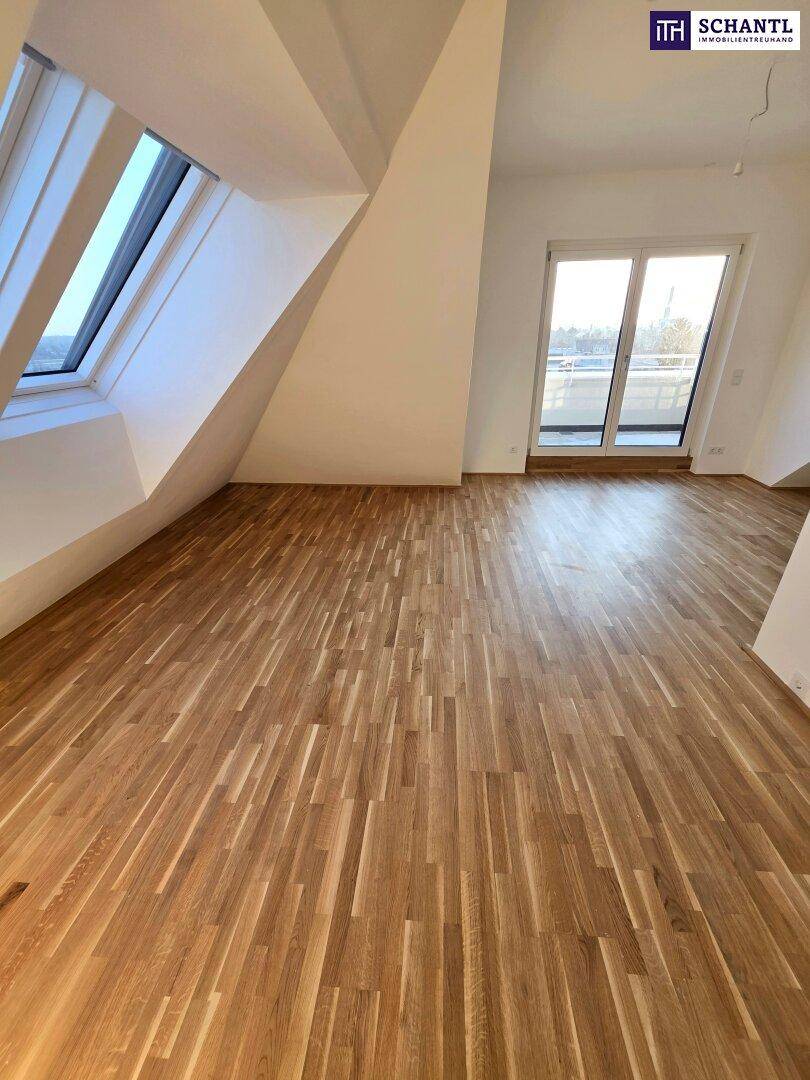 Geräumiges Zimmer im Dachgeschoss mit Holzboden und Zugang zu einem Balkon, hell durch Fenster.