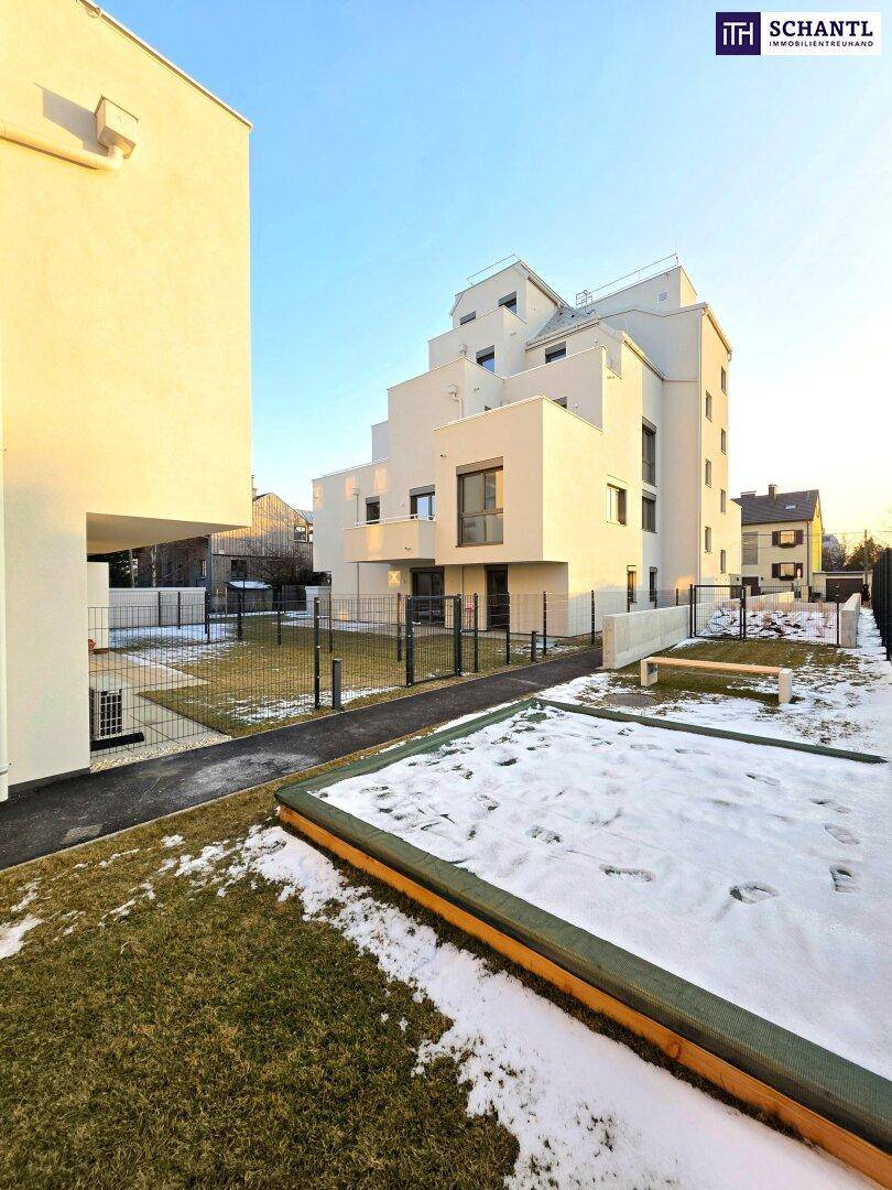 Moderne Wohnanlage mit umzäuntem Gartenbereich und Sandkasten, teilweise mit Schnee bedeckt.