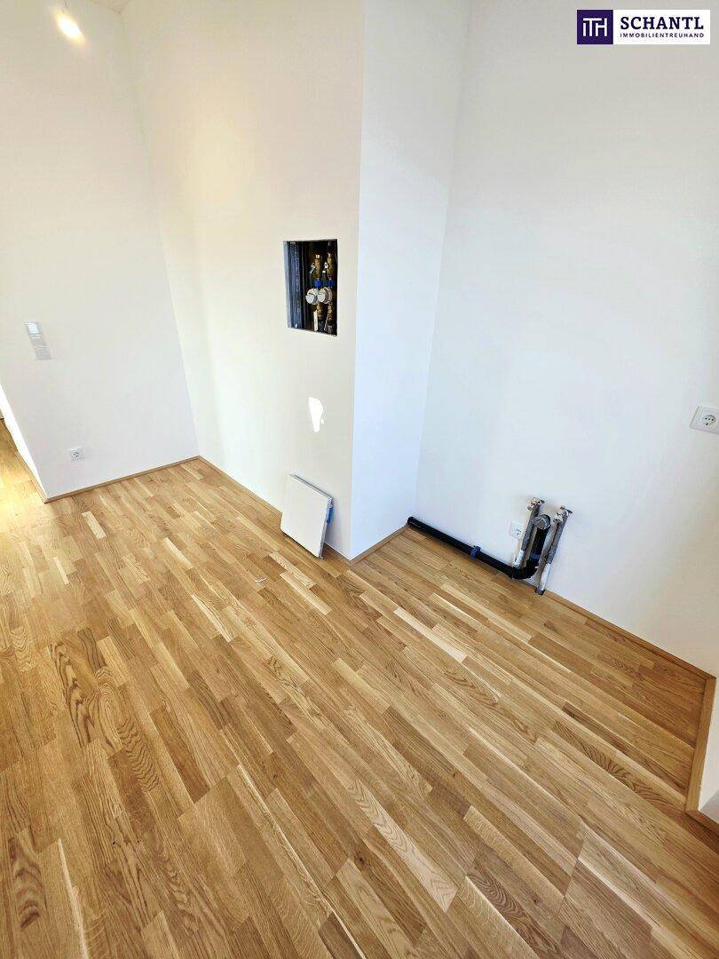 Leerer Raum mit Holzboden und sichtbaren Anschlüssen, bereit für die Kücheninstallation.