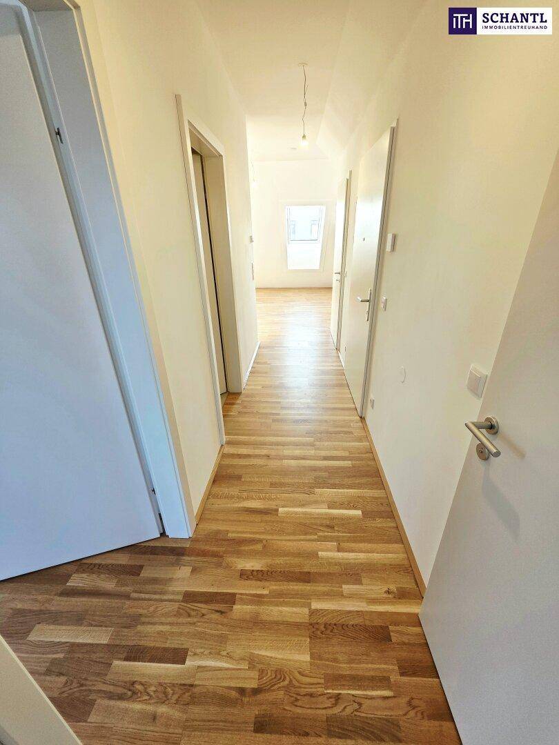 Heller Flur mit Holzboden und weißen Wänden, der zu weiteren Räumen führt.