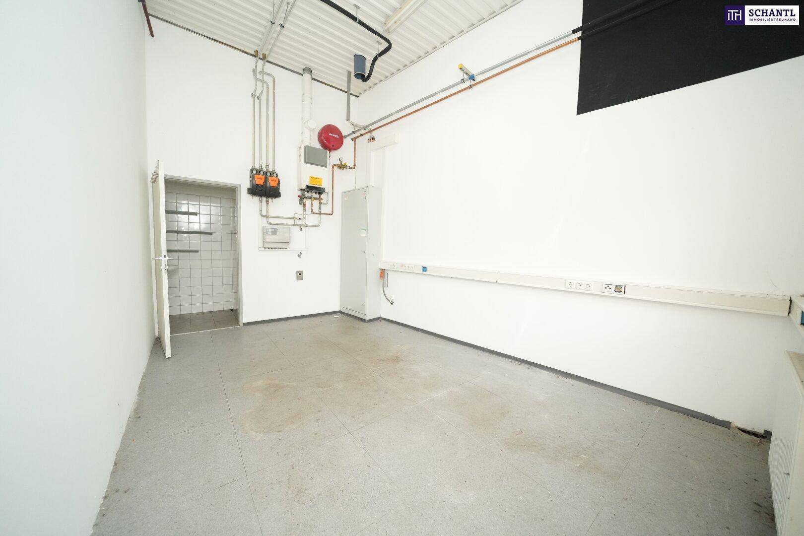 Heller Technikraum mit weißen Wänden, sichtbaren Rohren und Zugang zu einem gefliesten Sanitärbereich.