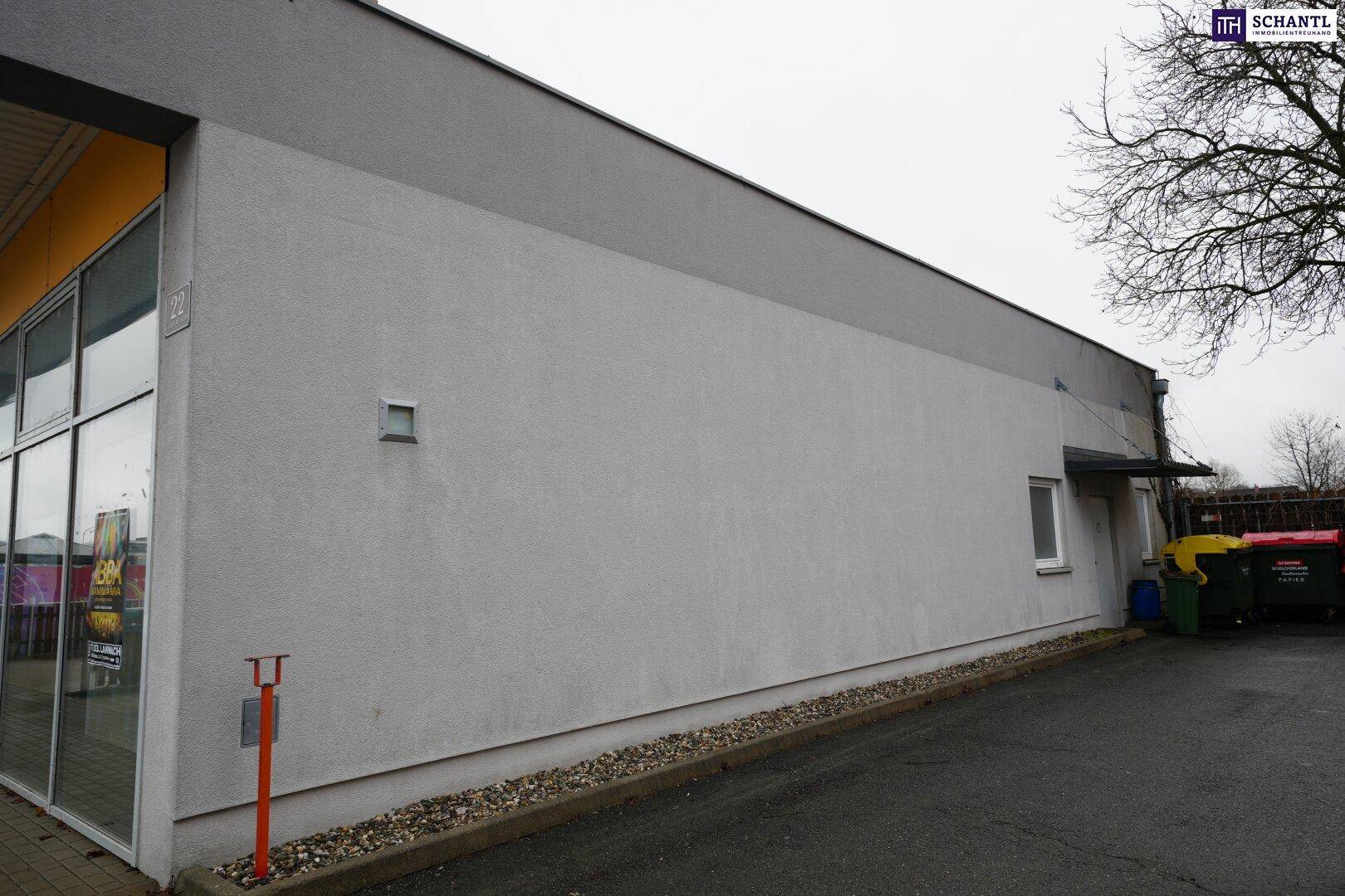 Seitenansicht des Gebäudes mit schlichter Fassade und einem kleinen Fenster, angrenzend an den Parkplatz.