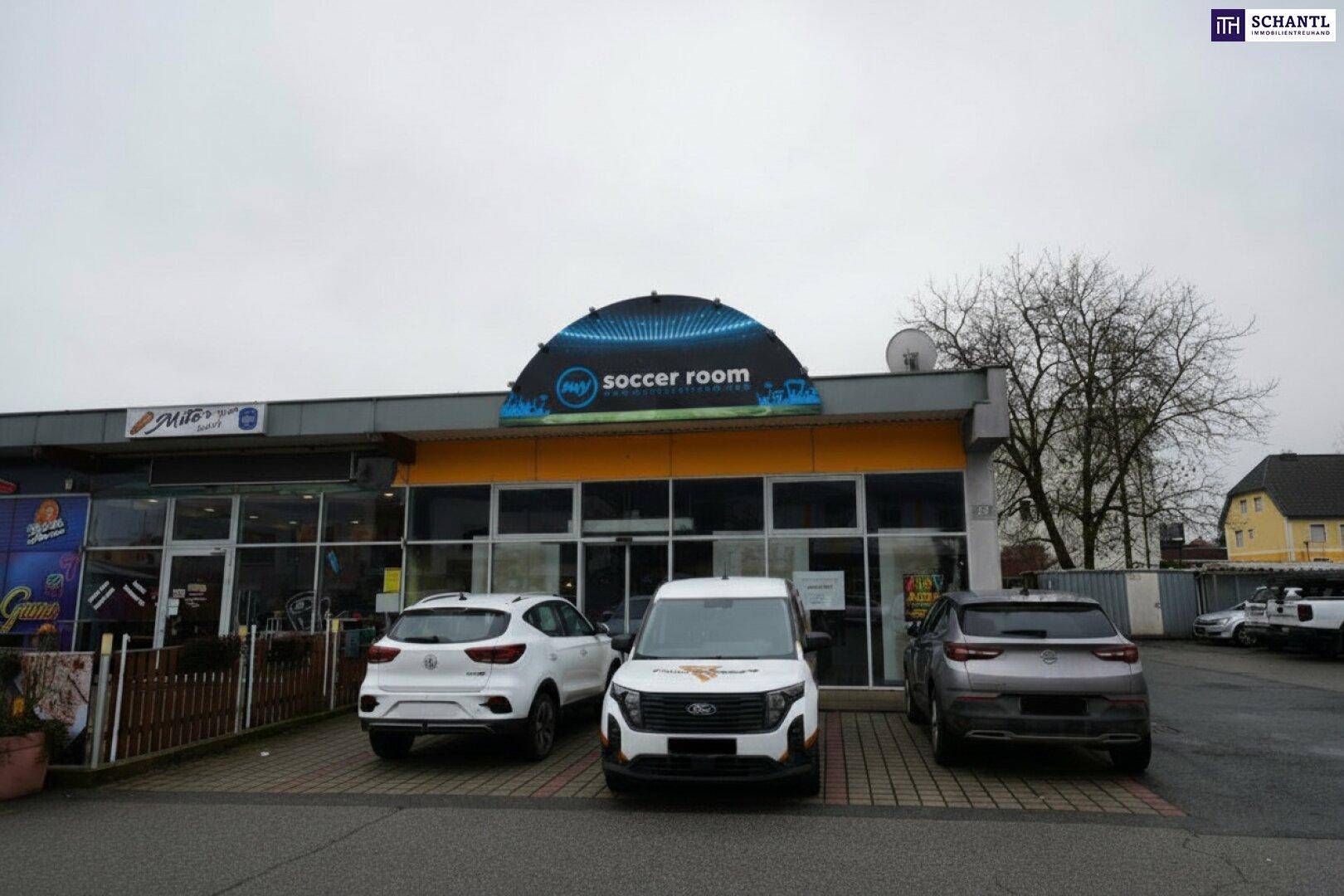 Vorderansicht des Geschäftsgebäudes mit großer Glasfront und Parkplätzen davor, unter bewölktem Himmel.