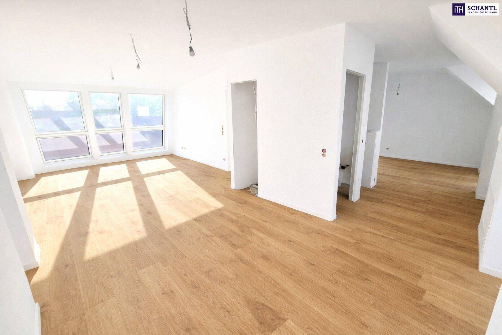 Heller, leerer Raum mit Holzboden und großen Fenstern, ideal als Wohnbereich in einem Dachgeschoss.