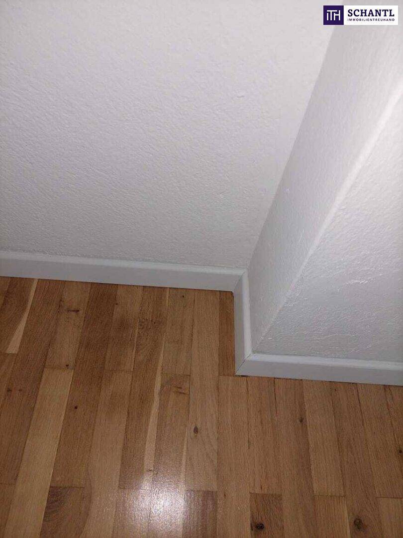 Detailansicht eines hellen Holzbodens und einer weißen Wand mit Fußleiste.