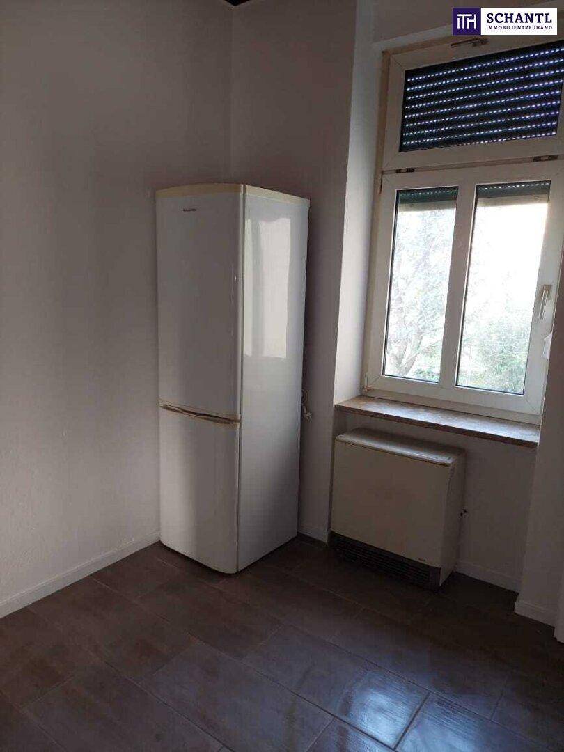 Raum mit dunklem Fliesenboden, Kühlschrank und Fenster mit Rollladen.