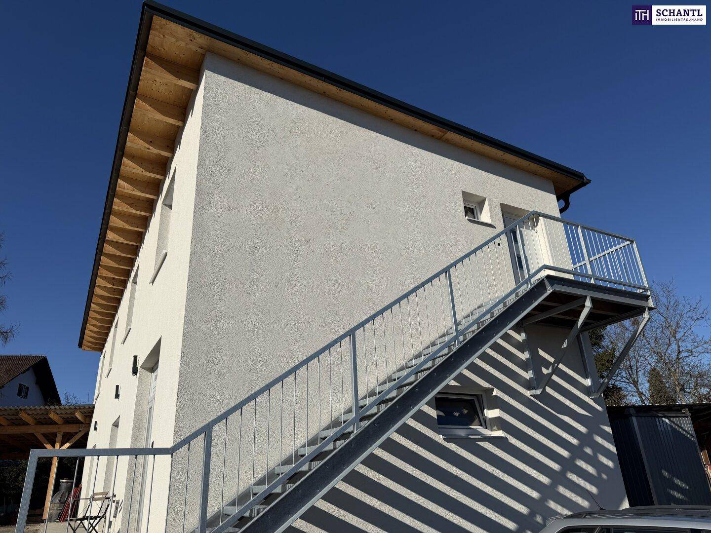 Ansicht des modernen Neubaus mit weißer Fassade, schrägem Dach und einer freistehenden Außentreppe zum Balkon.