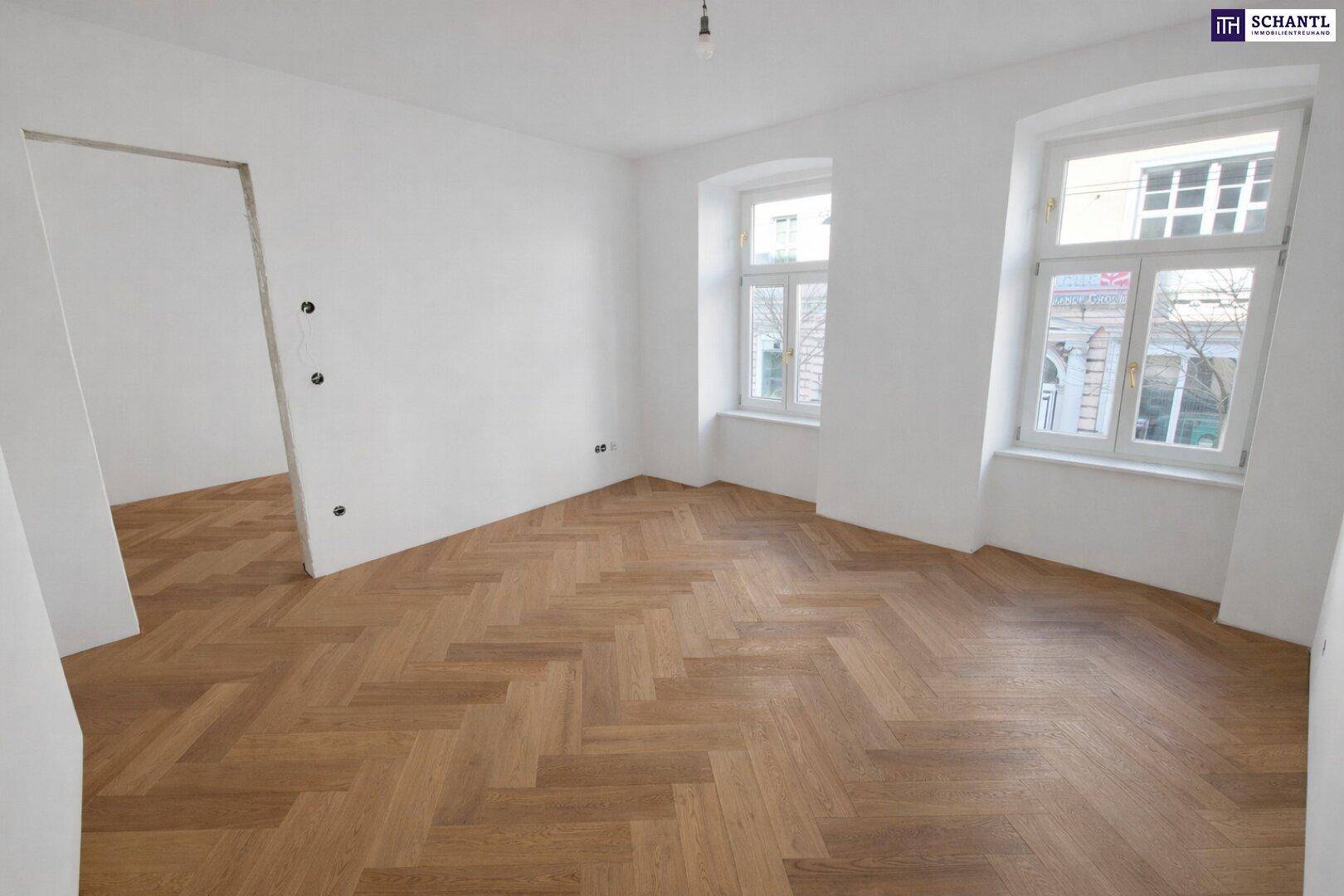 Lichtdurchfluteter Raum mit elegantem Fischgrätparkett und zwei Fenstern, ideal für Wohnzwecke.