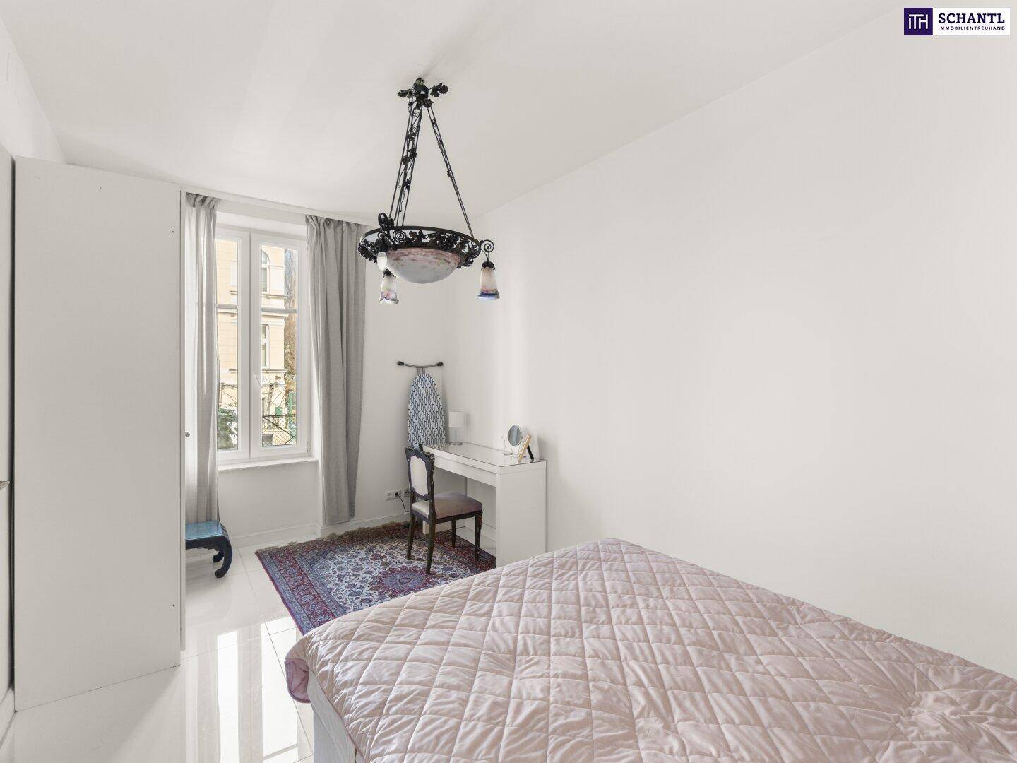 Helles Schlafzimmer mit Fenster, Schrank und einem Schreibtisch.