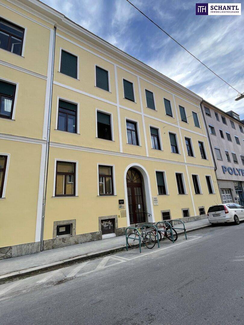 Gelbes Mehrfamilienhaus mit klassischer Architektur und vielen Fenstern an einer belebten Straße.