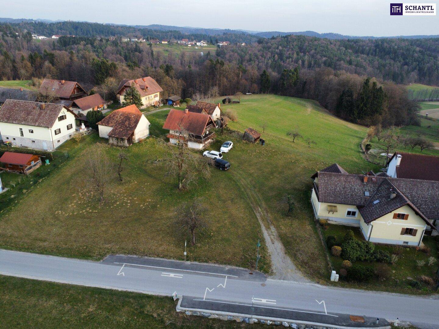 Luftaufnahme eines ländlichen Wohngebiets mit mehreren Häusern und grünen Hügeln im Hintergrund.