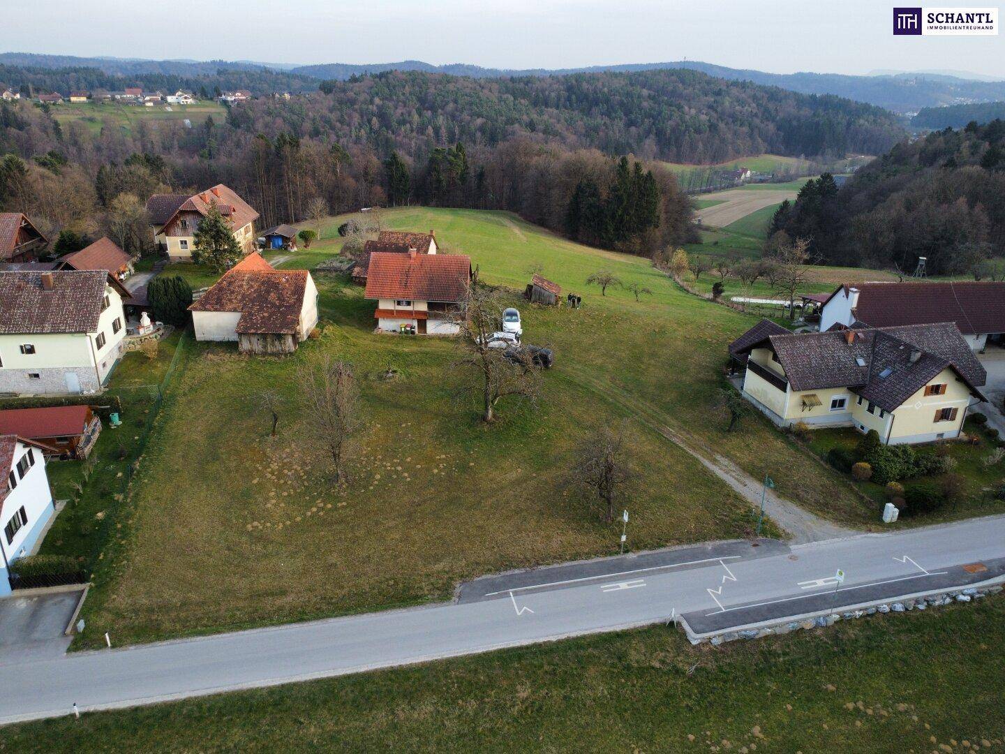 Übersicht aus der Vogelperspektive auf ein Grundstück mit angrenzenden Häusern und bewaldeten Hügeln.