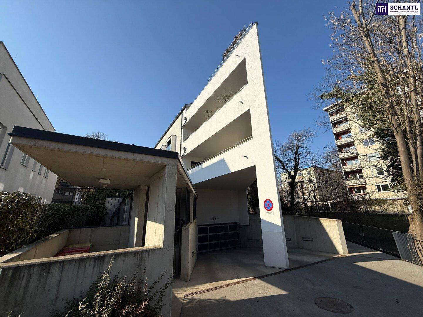 Auffälliges modernes Wohnhaus mit mehreren Balkonen und einer Zufahrt zur Tiefgarage unter blauem Himmel.