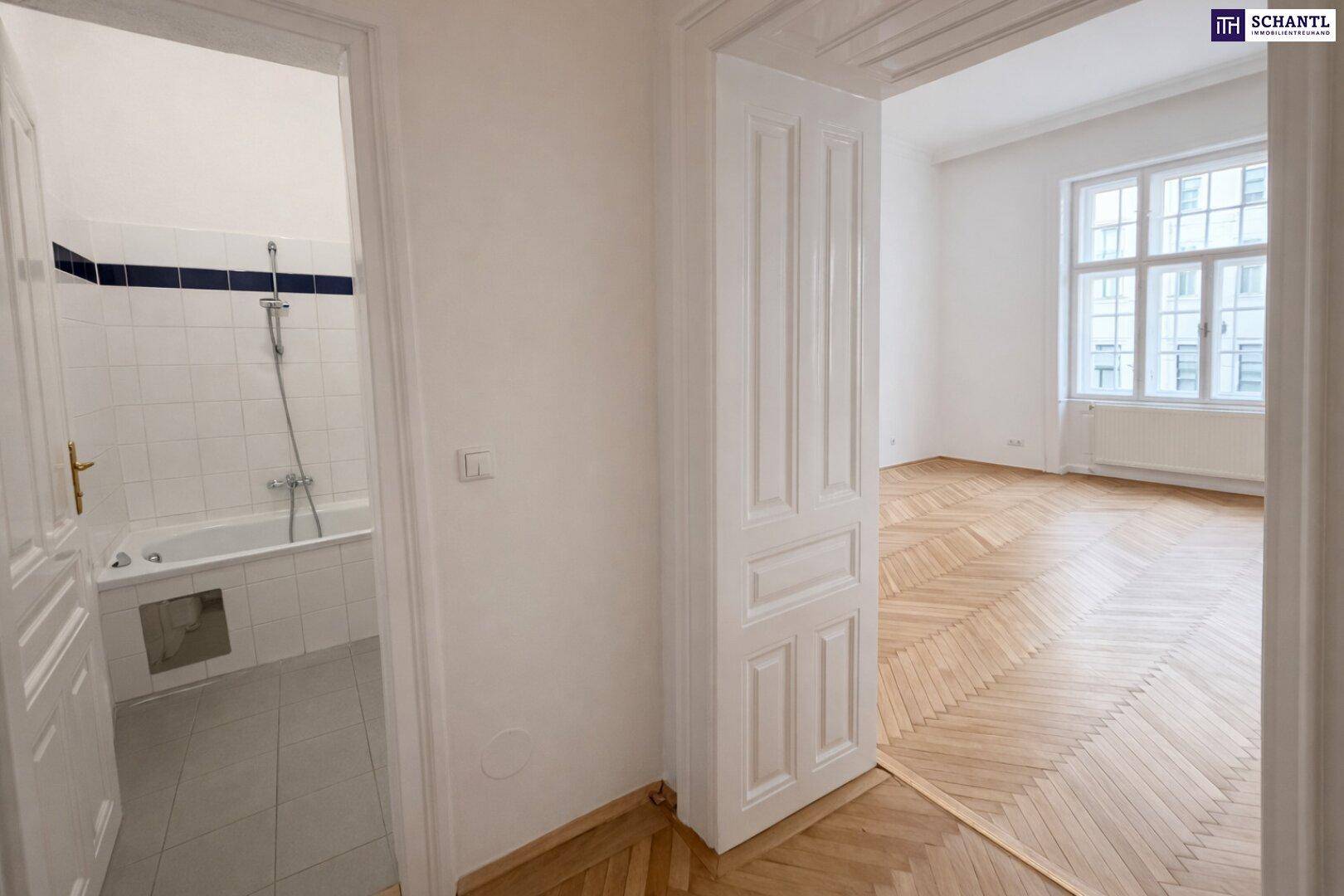 Blick aus dem Badezimmer in einen hellen, leeren Raum mit Fischgrätparkettboden.