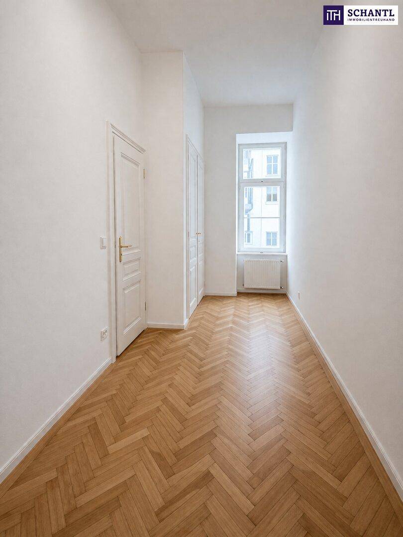 Langer, heller Flur mit Fischgrätparkett und einem Fenster, bietet Zugang zu weiteren Räumen.