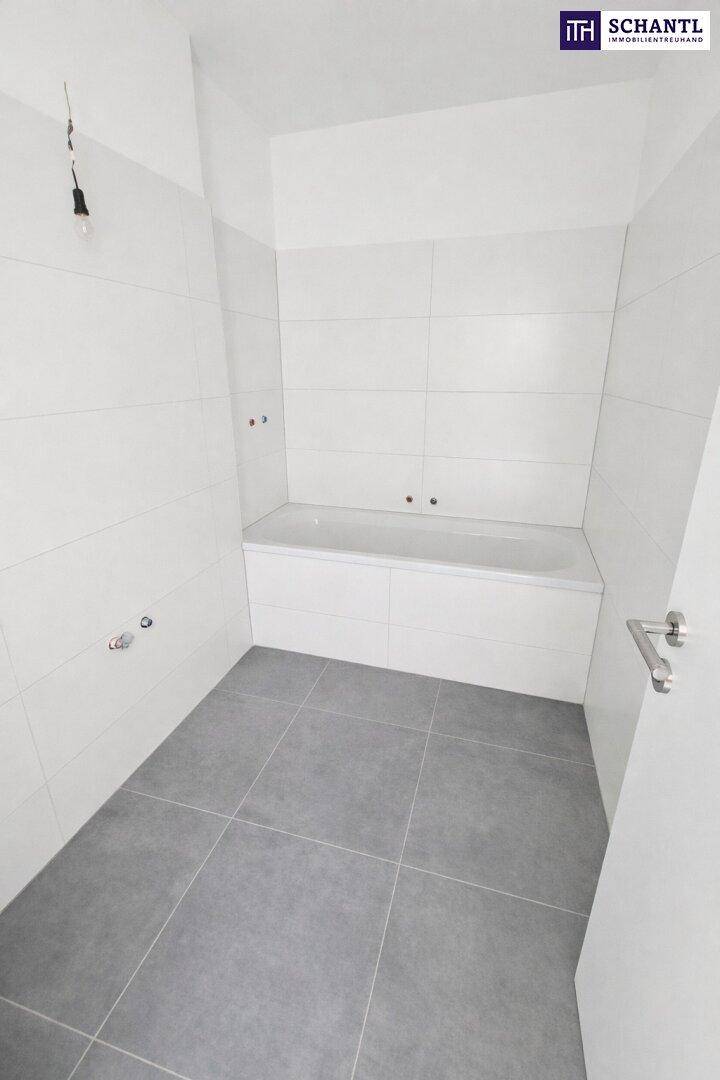 Helles Badezimmer mit Badewanne und weißen Wand- und grauen Bodenfliesen.