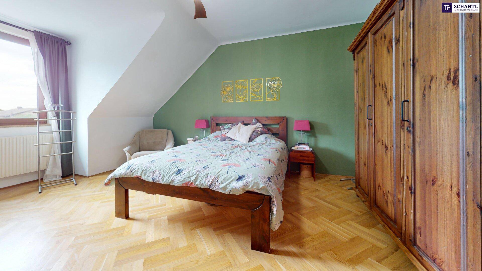 Schlafzimmer mit grüner Akzentwand, Holzbett und Parkettboden unter Dachschräge.