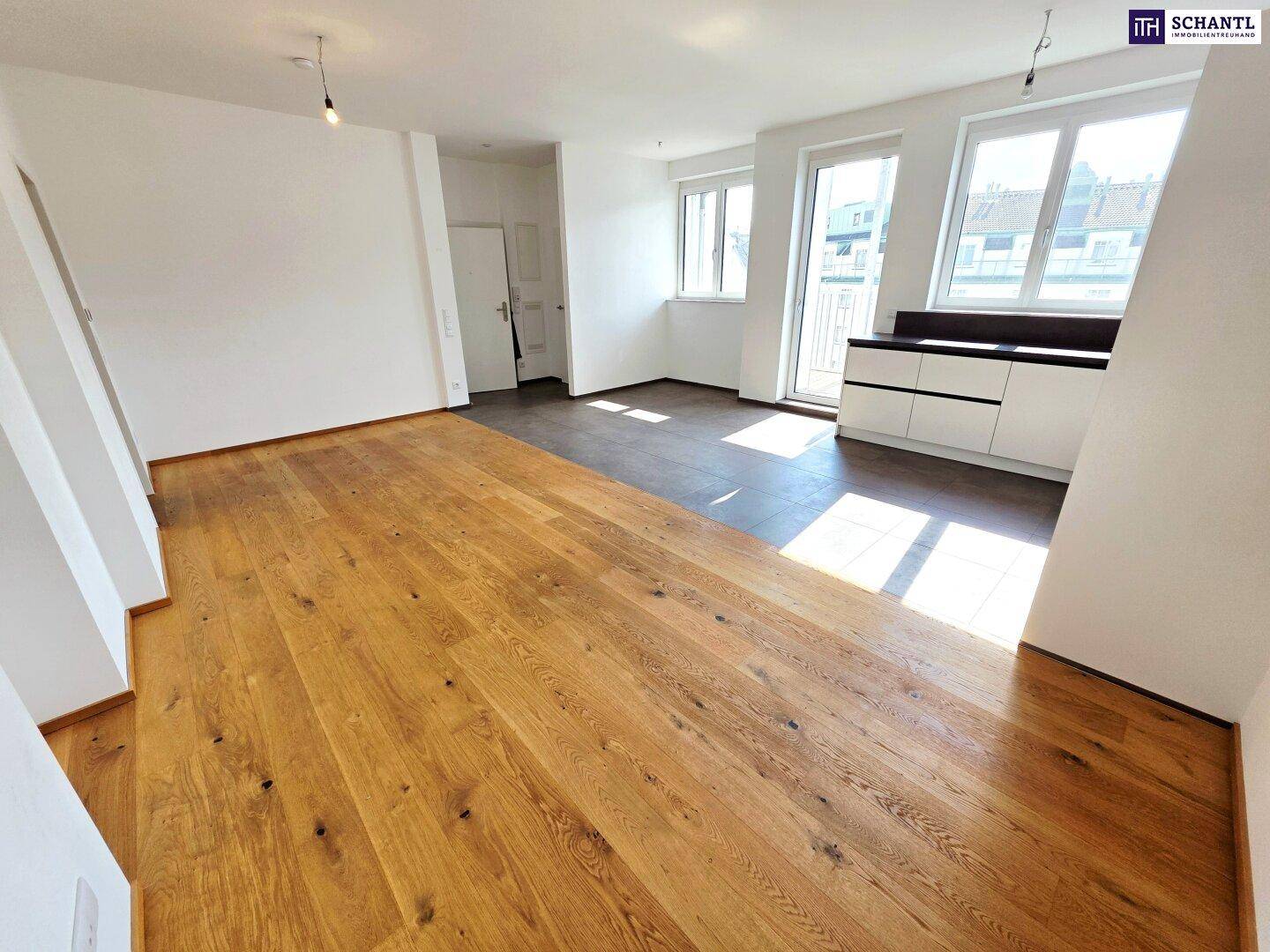 Lichtdurchfluteter Wohnbereich mit integrierter Küche, Holzboden und Zugang zum Balkon.