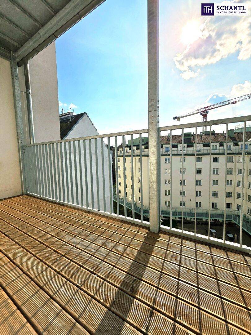 Sonniger Balkon mit Holzdielen und Blick auf den Innenhof mit Grünflächen.