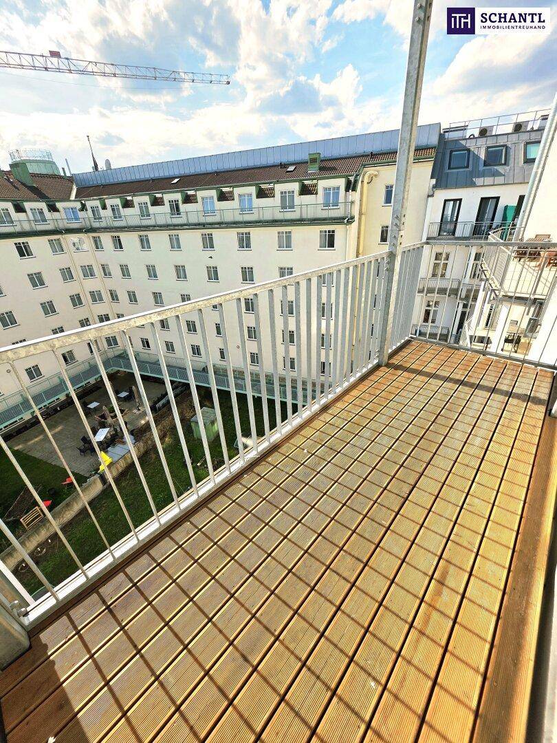 Heller Balkon mit Holzboden und weitem Blick über den Innenhofbereich.