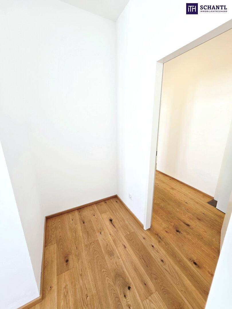 Leerer Raum mit Holzboden und weiß gestrichenen Wänden, mit offenem Durchgang.