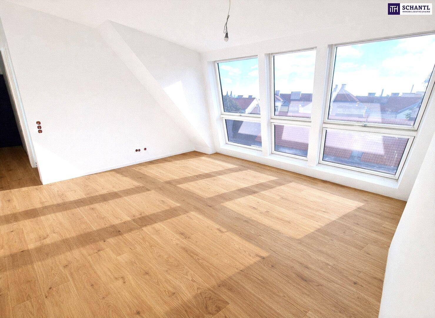 Heller Raum im Dachgeschoss mit Holzfußboden und großen Fenstern mit Blick über die Dächer.