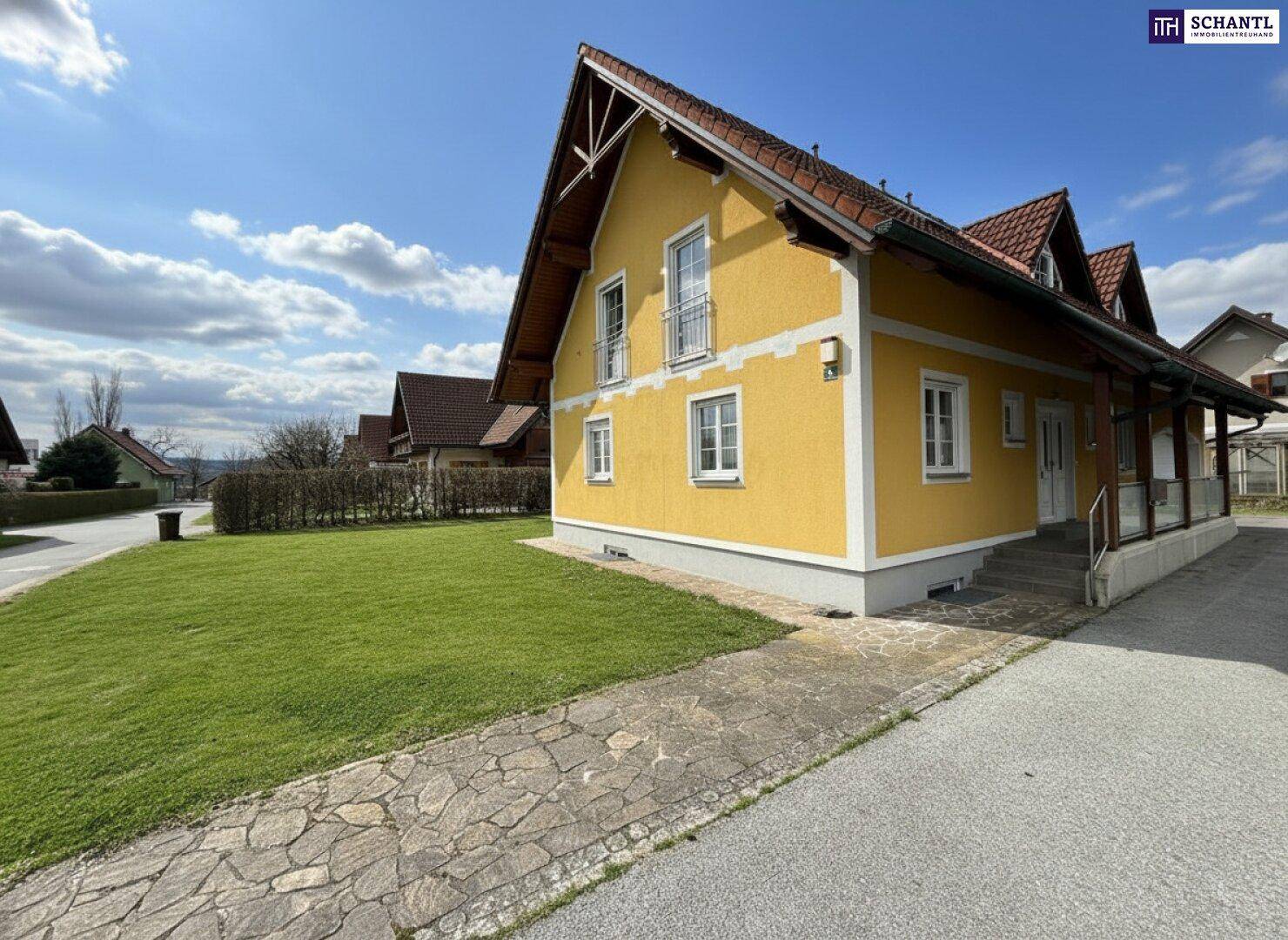 Seitenansicht des Hauses mit gelber Fassade, gepflegtem Rasen und Zufahrt an einem sonnigen Tag.