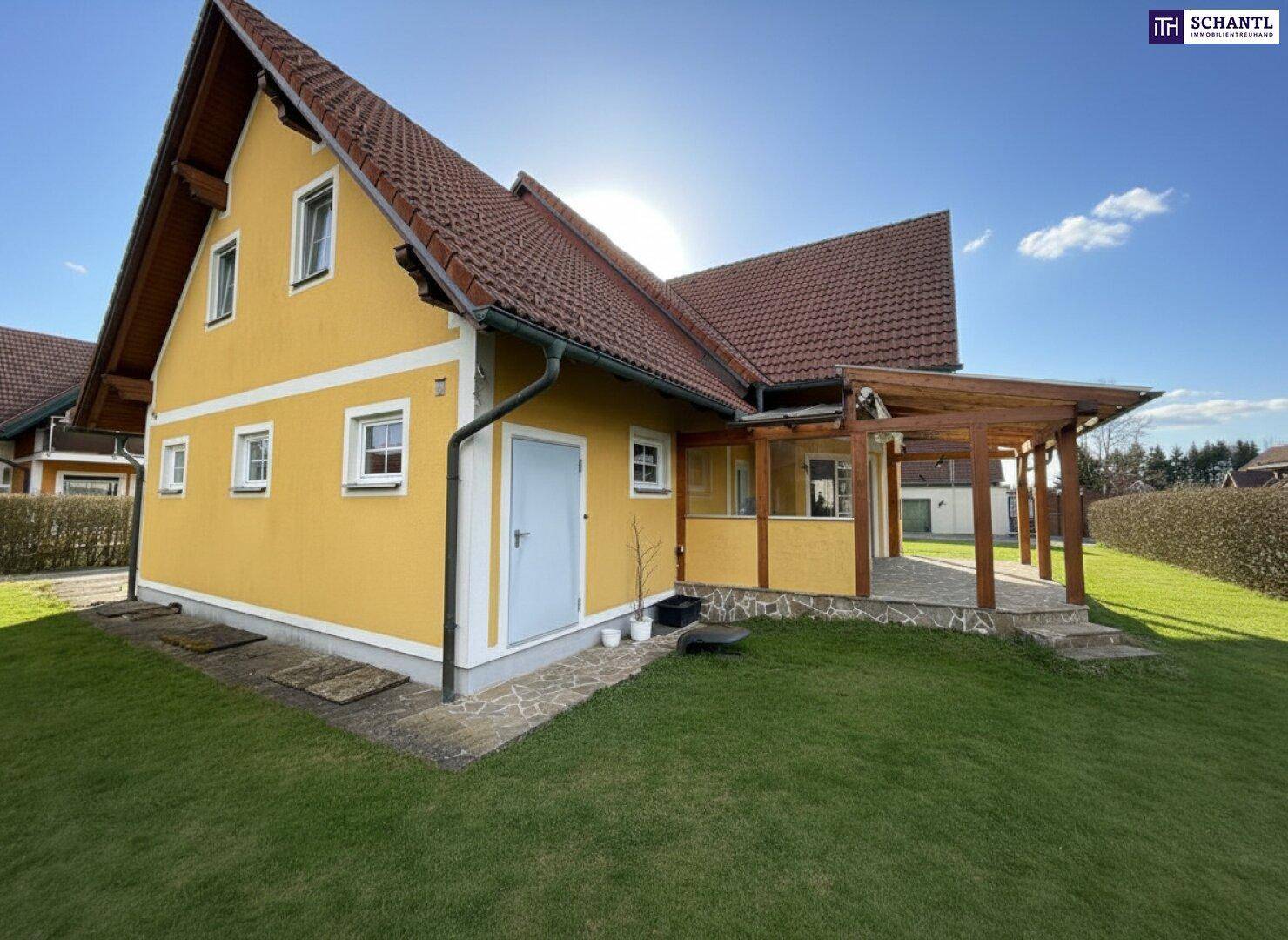 Seitenansicht des Hauses mit gelber Fassade, Nebeneingang und gepflegtem Rasen.