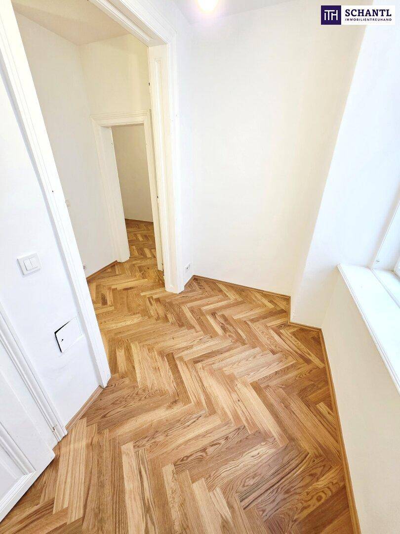 Langer Flur mit Fischgrätparkett, der zu weiteren Zimmern der Wohnung führt.