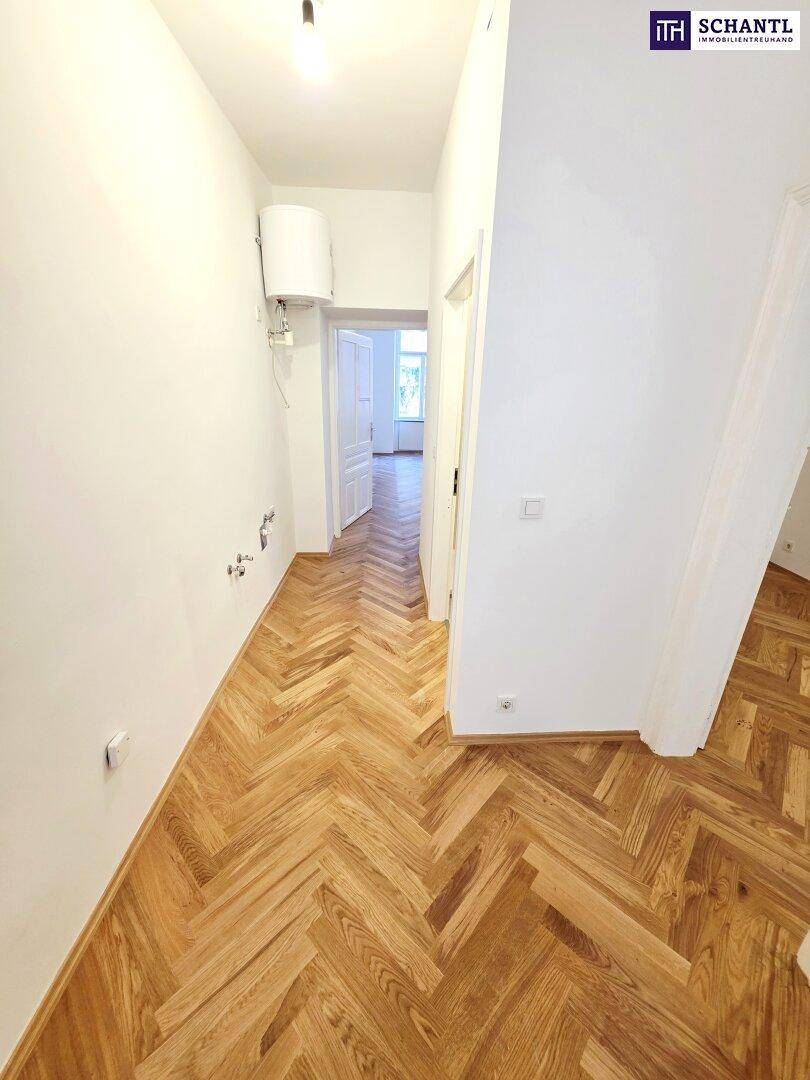 Flur mit Fischgrätparkett und sichtbaren Anschlüssen für eine zukünftige Küchenzeile oder Bad.