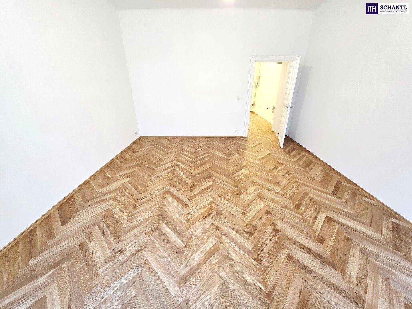 Leeres Zimmer mit Fischgrätparkett und weiß gestrichenen Wänden, bereit zum Einzug und zur individuellen Gestaltung.