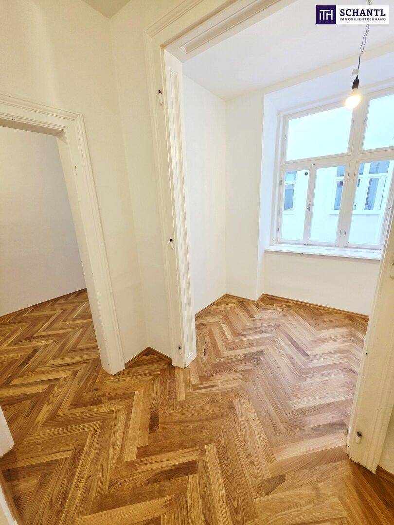 Helles Zimmer mit Fischgrätparkett und einem großen Fenster, das viel Licht hereinlässt.