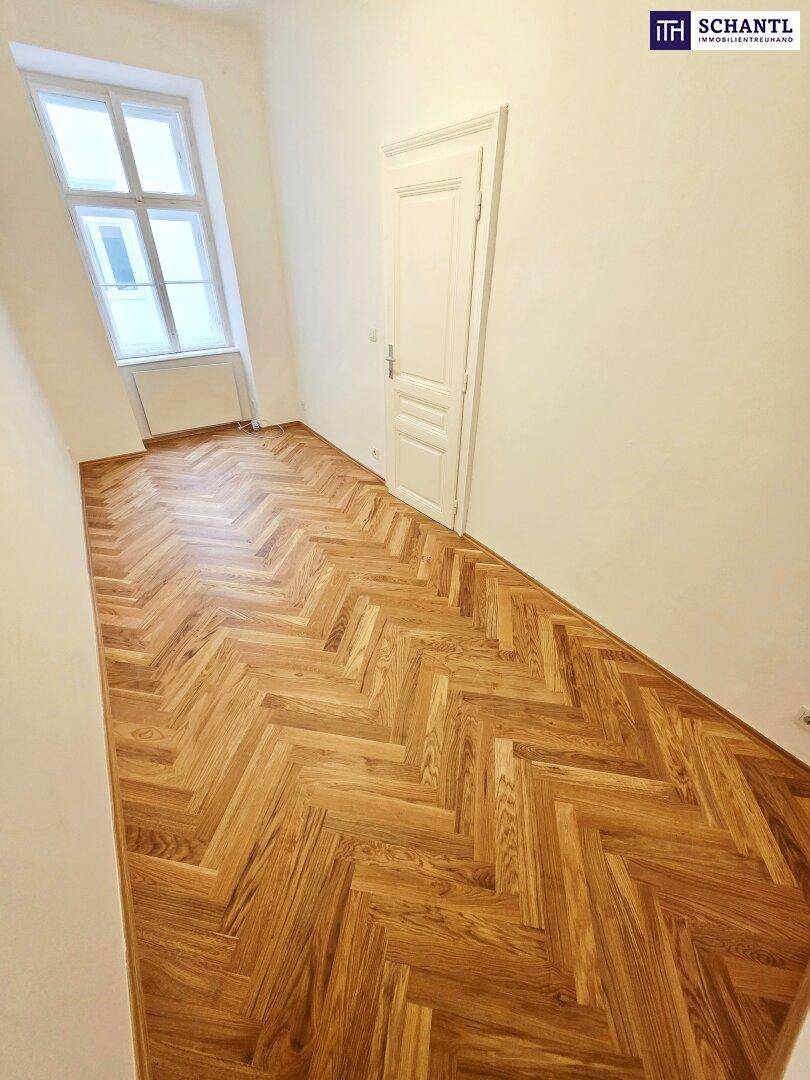 Geräumiges Zimmer mit Fischgrätparkett und einer hohen Tür, die den Altbaucharakter unterstreicht.