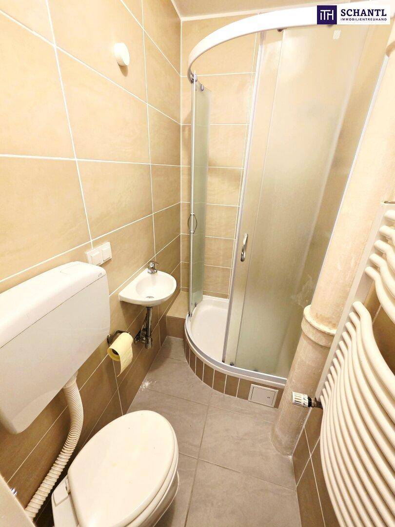 Kleines Badezimmer mit beigefarbenen Fliesen, Dusche, WC und Handtuchheizkörper.
