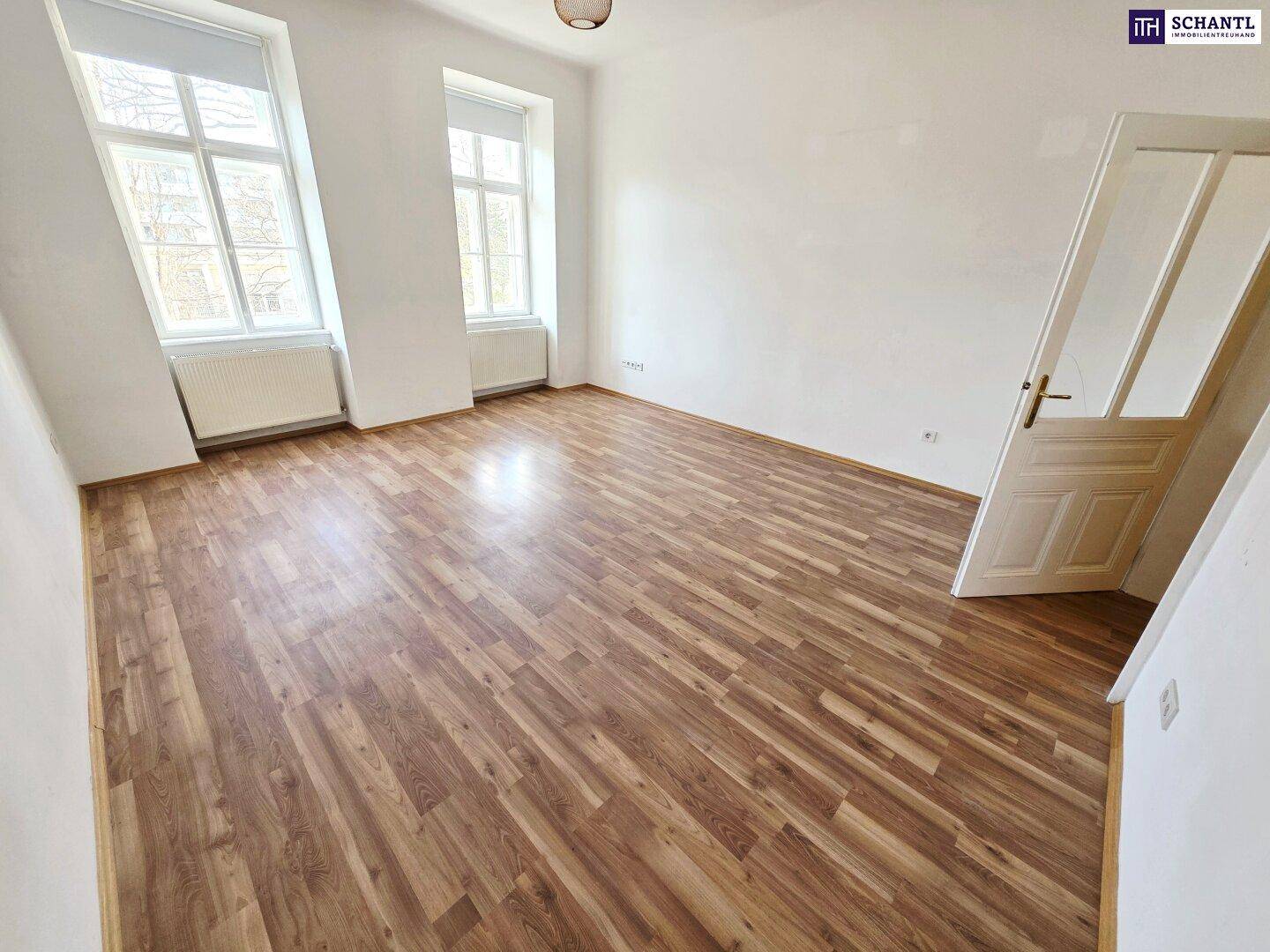 Geräumiges Zimmer mit Laminatboden, hohen Fenstern und viel Tageslicht.