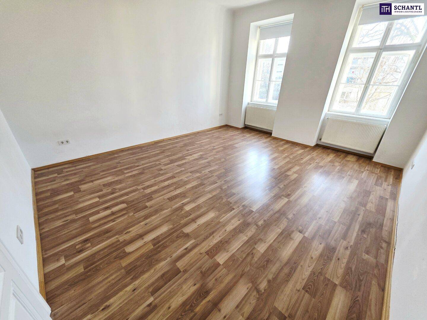 Helles Zimmer mit Laminatboden und zwei hohen Fenstern, ideal für Wohn- oder Schlafbereich.