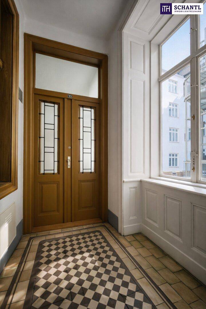 Historischer Eingangsbereich mit Holztüren, Schachbrettmuster-Fliesenboden und großen Fenstern.