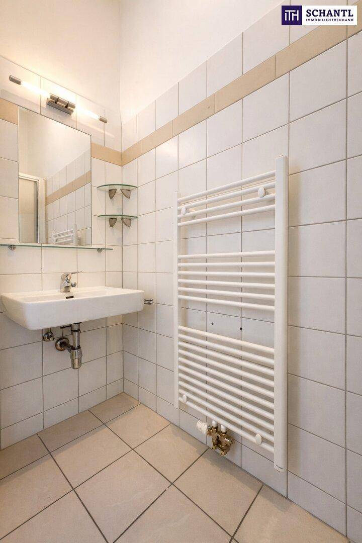Badezimmer mit weißen Fliesen, einem Waschbecken und einem beheizten Handtuchhalter.