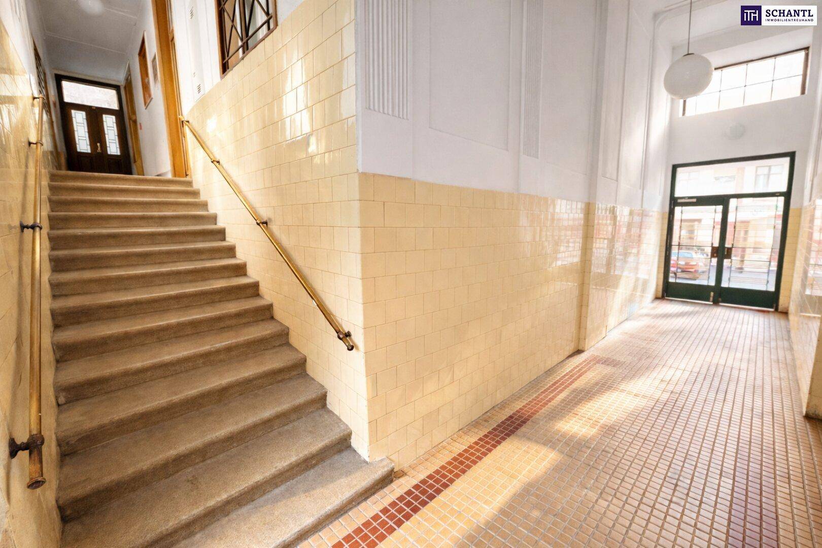 Geräumiges Treppenhaus mit gefliesten Wänden, einem Handlauf und einem Eingangsbereich mit Tageslicht.